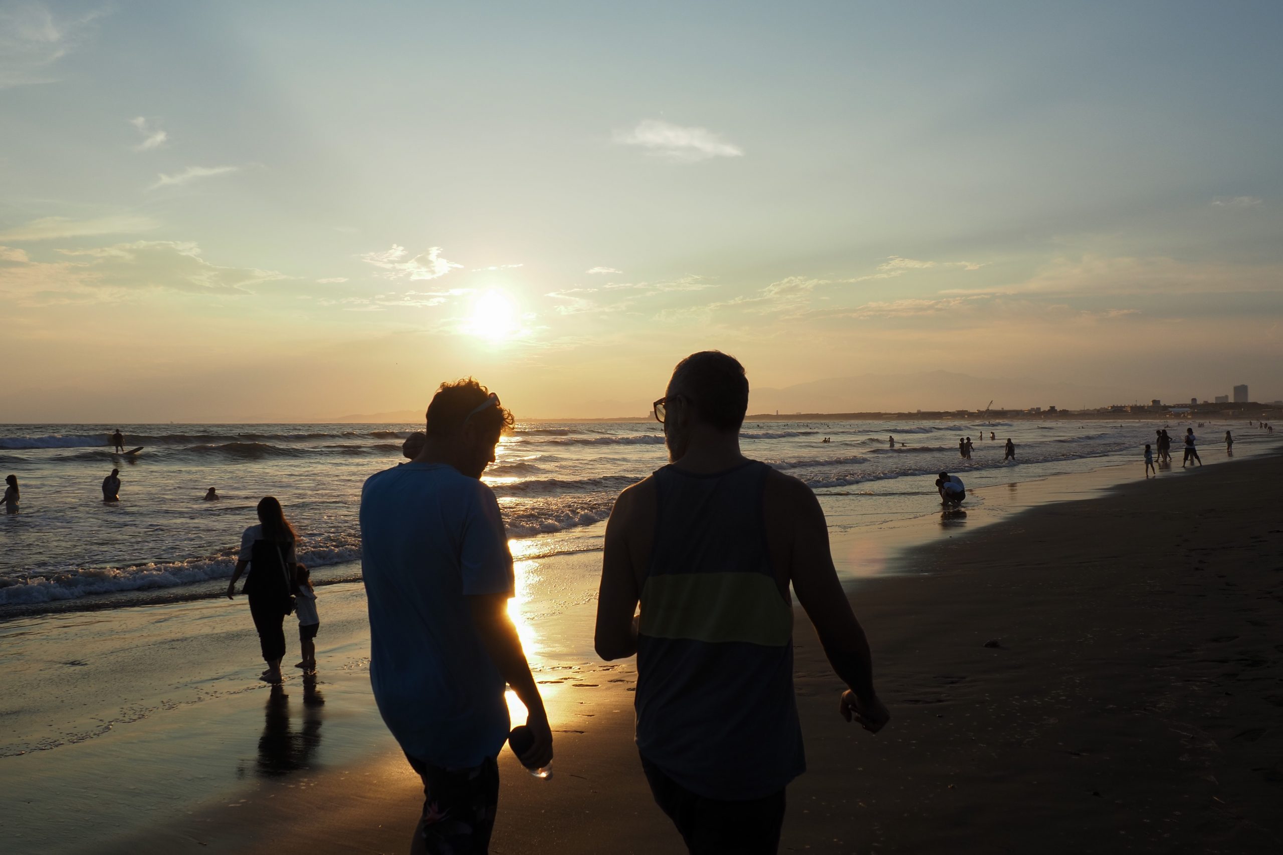 夕日を背に海辺を歩く人々を逆光で撮影